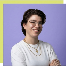 Smiling person with short dark hair, glasses, and a grey shirt against lavender background.