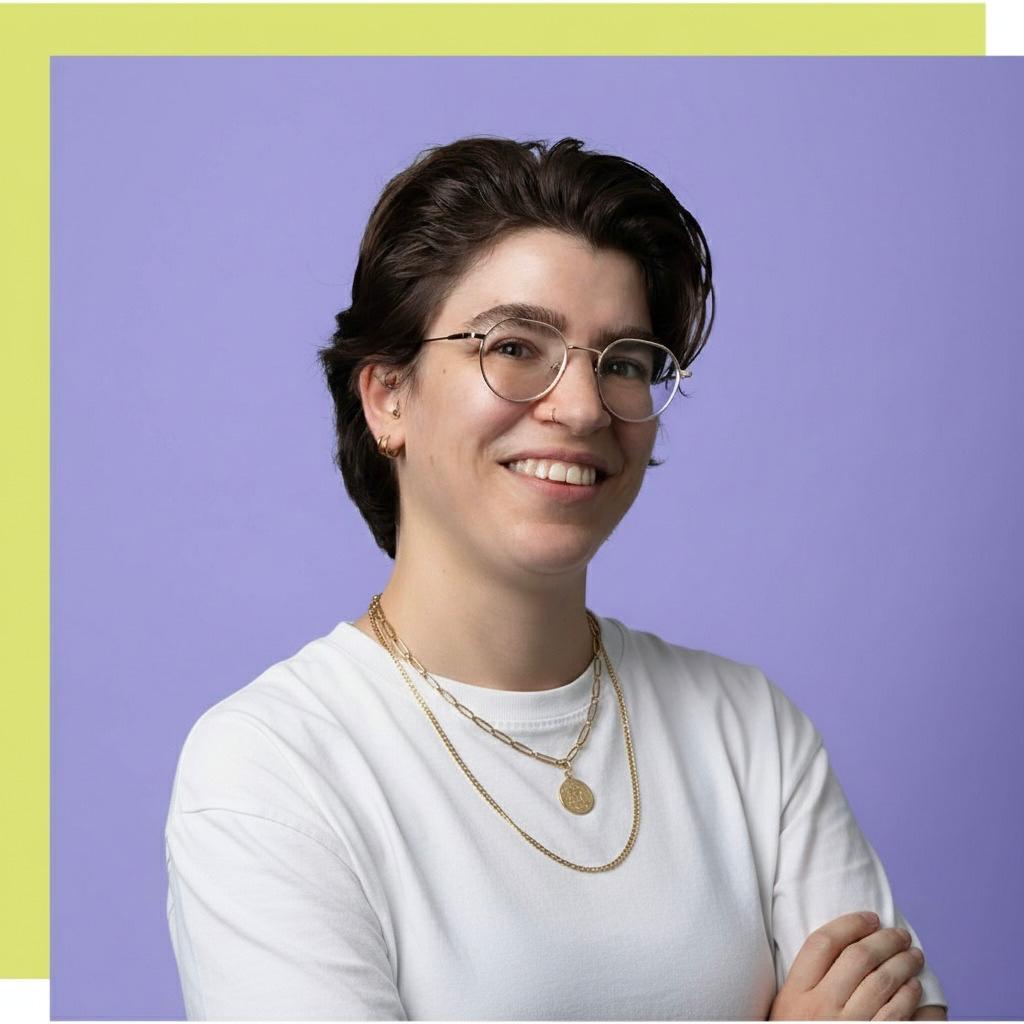 Smiling person with short dark hair, glasses, and a grey shirt against lavender background.